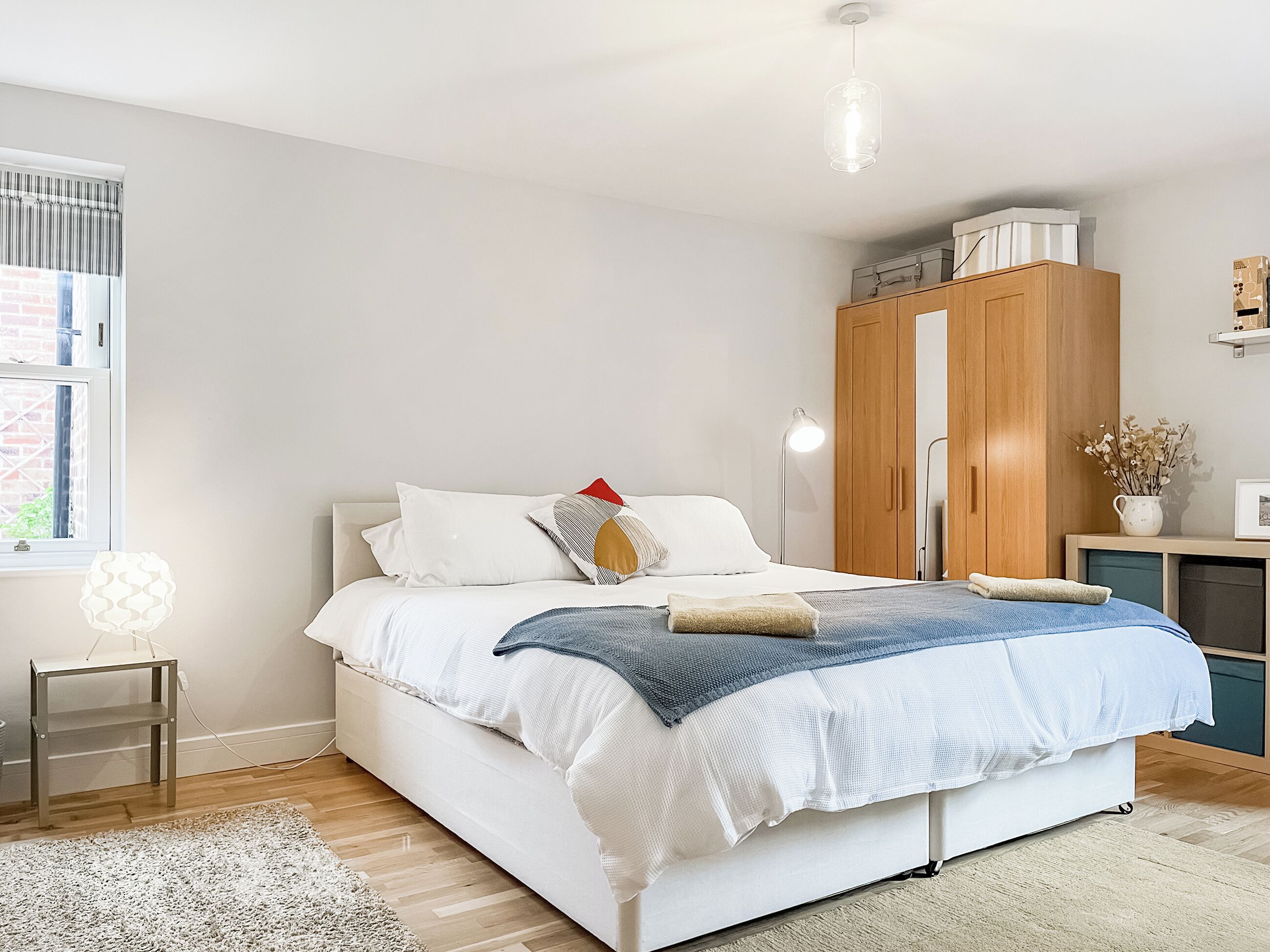 A modern bedroom with a bed, bedside lamp, wardrobe, and a small table.