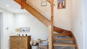 A wooden staircase with a handrail, a wooden cabinet, a wicker chair, and a small table with decorative items.