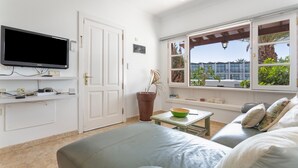Una sala de estar moderna con una televisión de pantalla plana, un ventanal con vistas a zonas verdes, un ventilador de techo y un espacio de descanso acogedor.