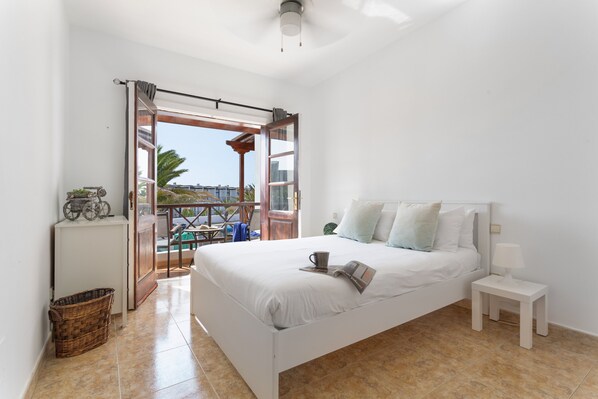 A bedroom with a bed, a nightstand, a window with curtains, a small table, and a view of the outside.