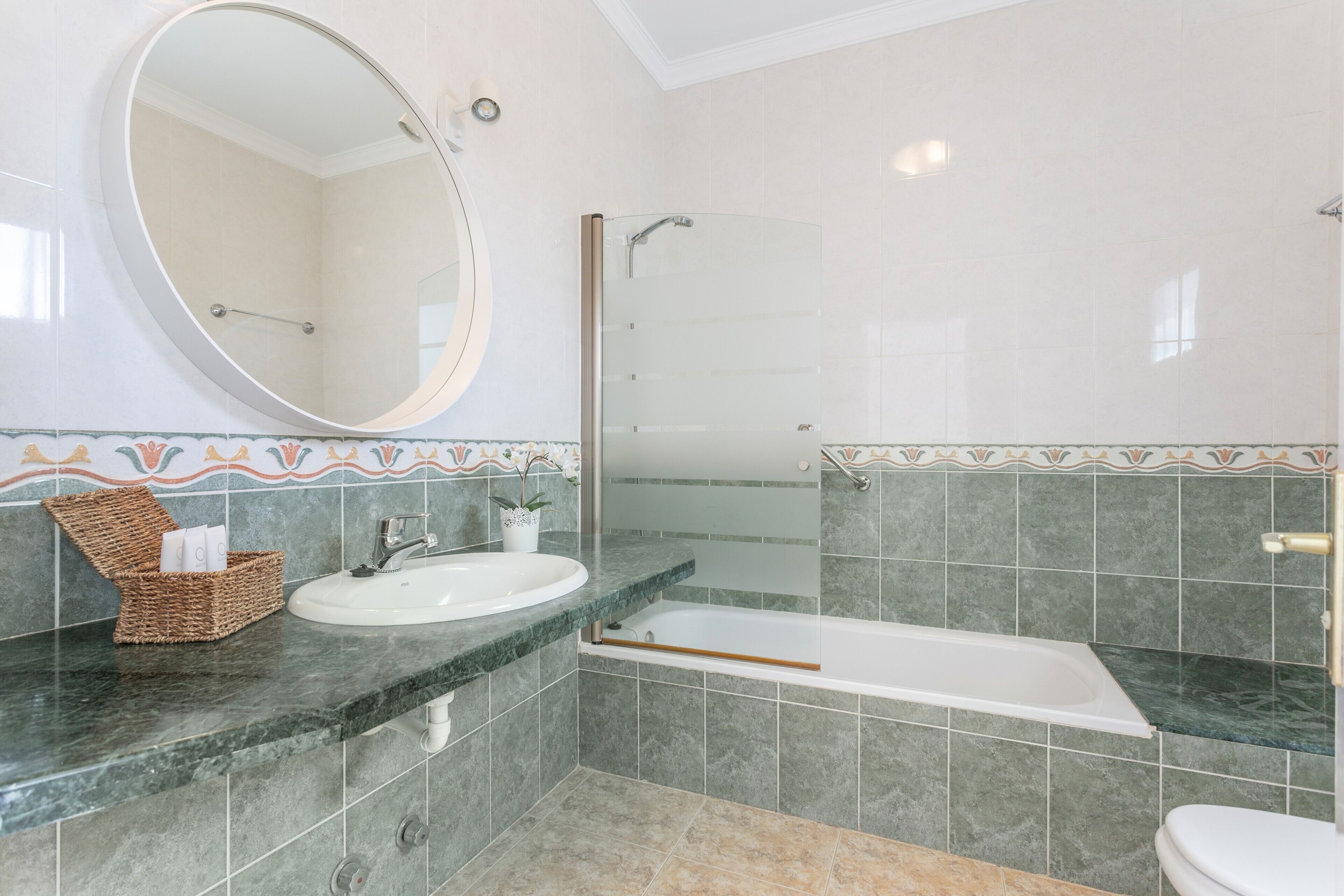 A bathroom with a round mirror, a sink, a bathtub, and a toilet.