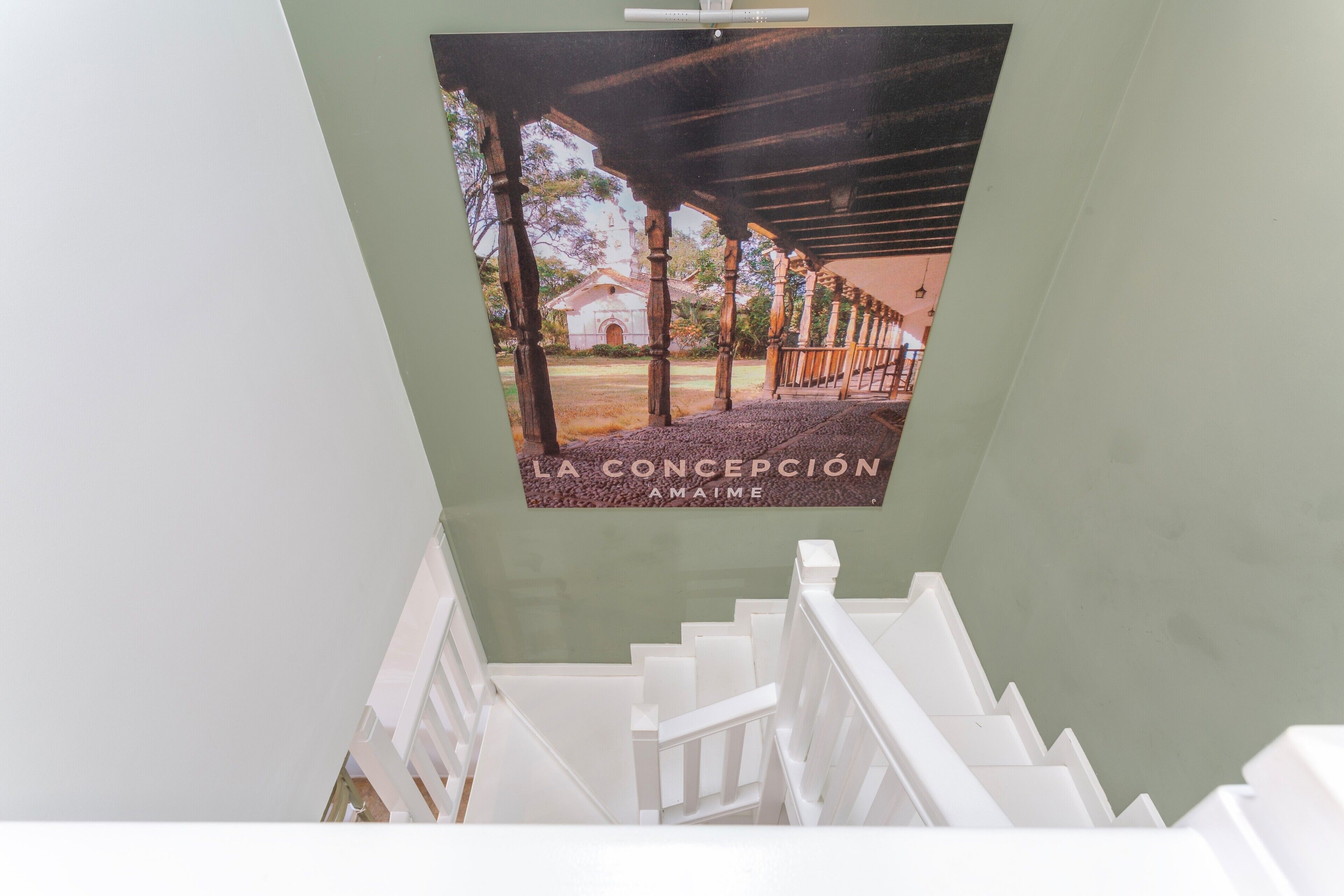 A staircase with white railings leading to a room with a green wall and a poster of a building.