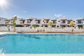A swimming pool with lounge chairs and a row of white buildings with balconies.