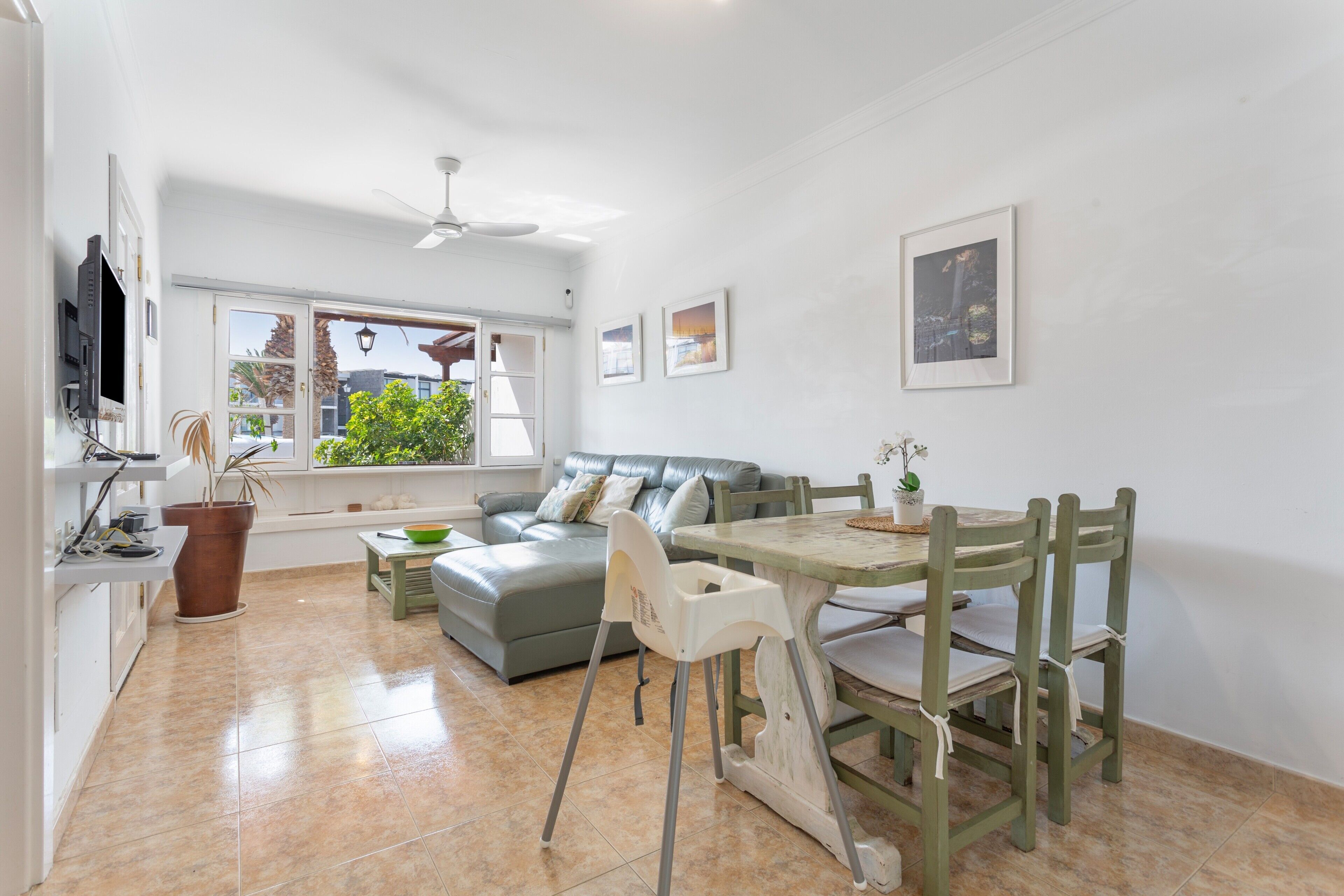 A spacious living area with a sofa, dining table, chairs, a television, and a window with a view of greenery.