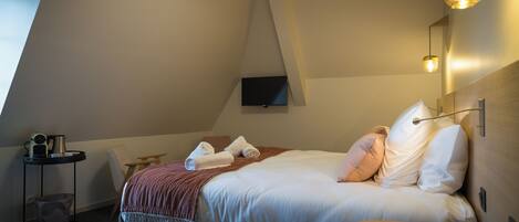 Una habitación de hotel moderna con una cama, una mesita pequeña, un televisor montado en la pared y un techo inclinado único.