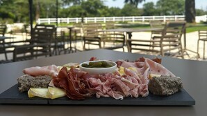 A table with a charcuterie board featuring various meats and cheeses, set outdoors with umbrellas and chairs. - Domaine de l'Ecorcerie (Liguge)