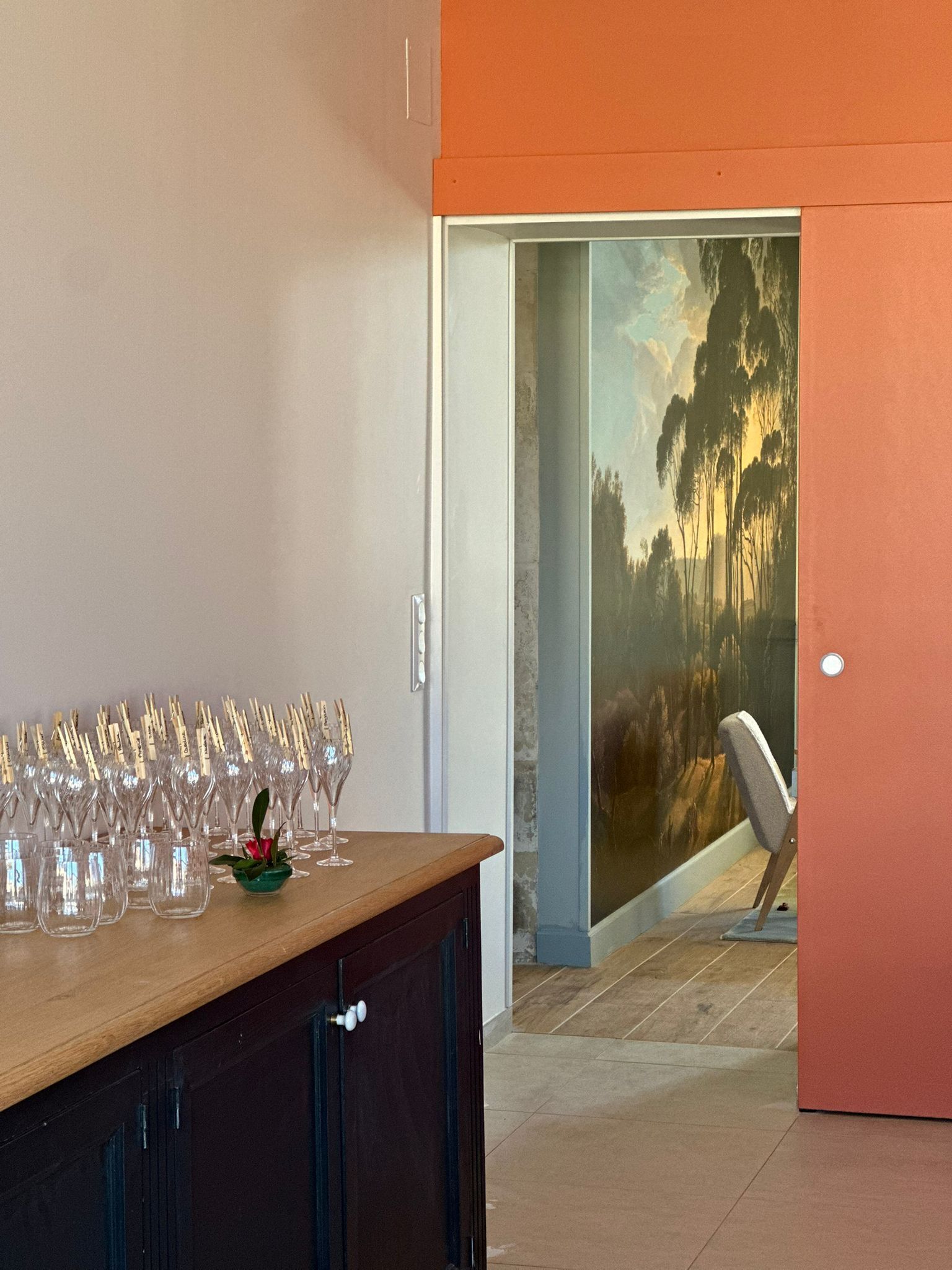 A room with a wooden bar area, a door leading to a room with a mural, and a chair.
