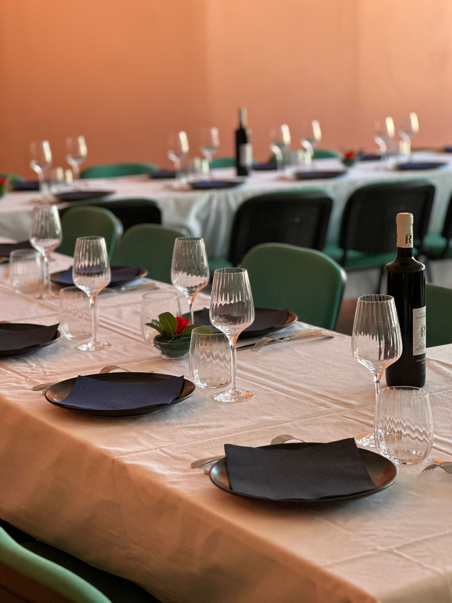 A dining table set with plates, glasses, and a bottle of wine, surrounded by green chairs.