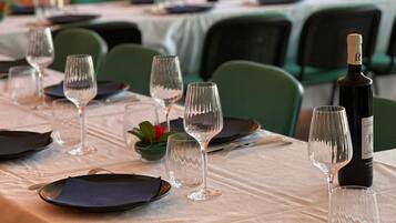 A dining table set with plates, glasses, and a bottle of wine, surrounded by green chairs.