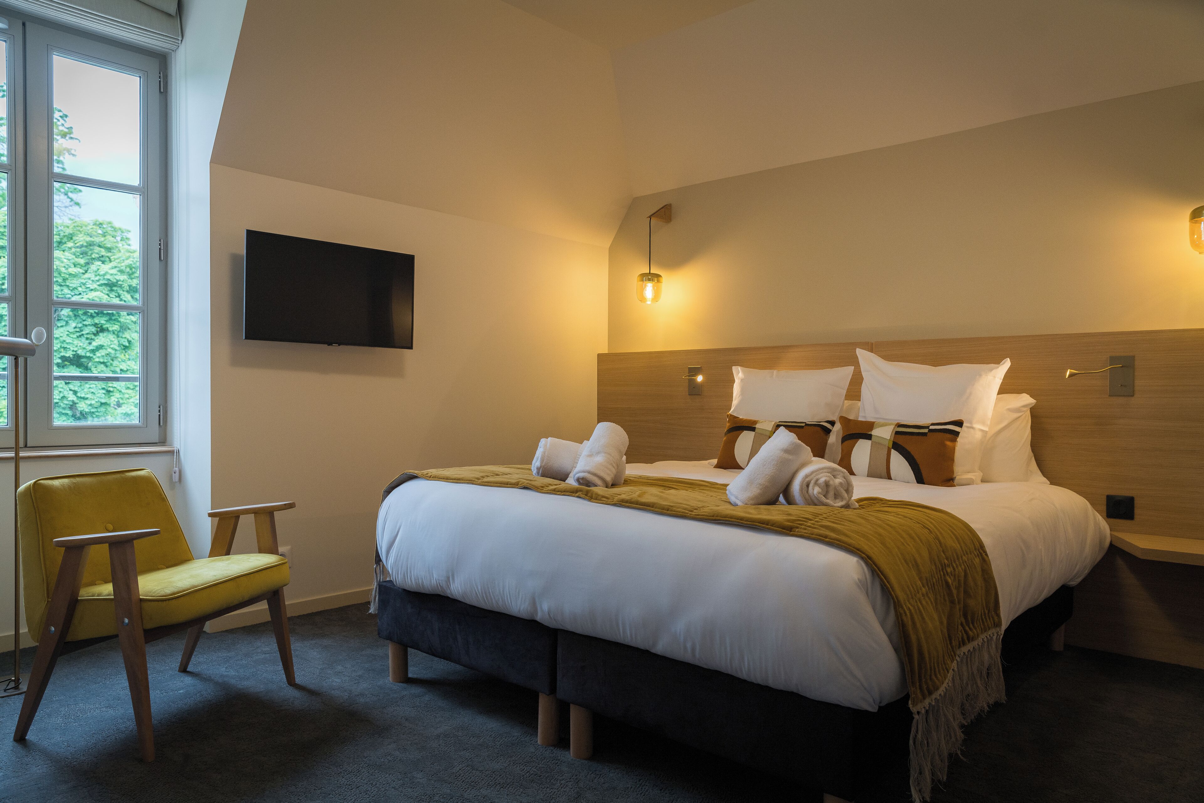 A hotel room with a bed, a chair, a TV, and a window.