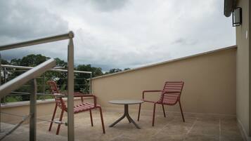 Un balcon avec deux chaises rouges et une petite table, donnant sur un jardin et un ciel nuageux.