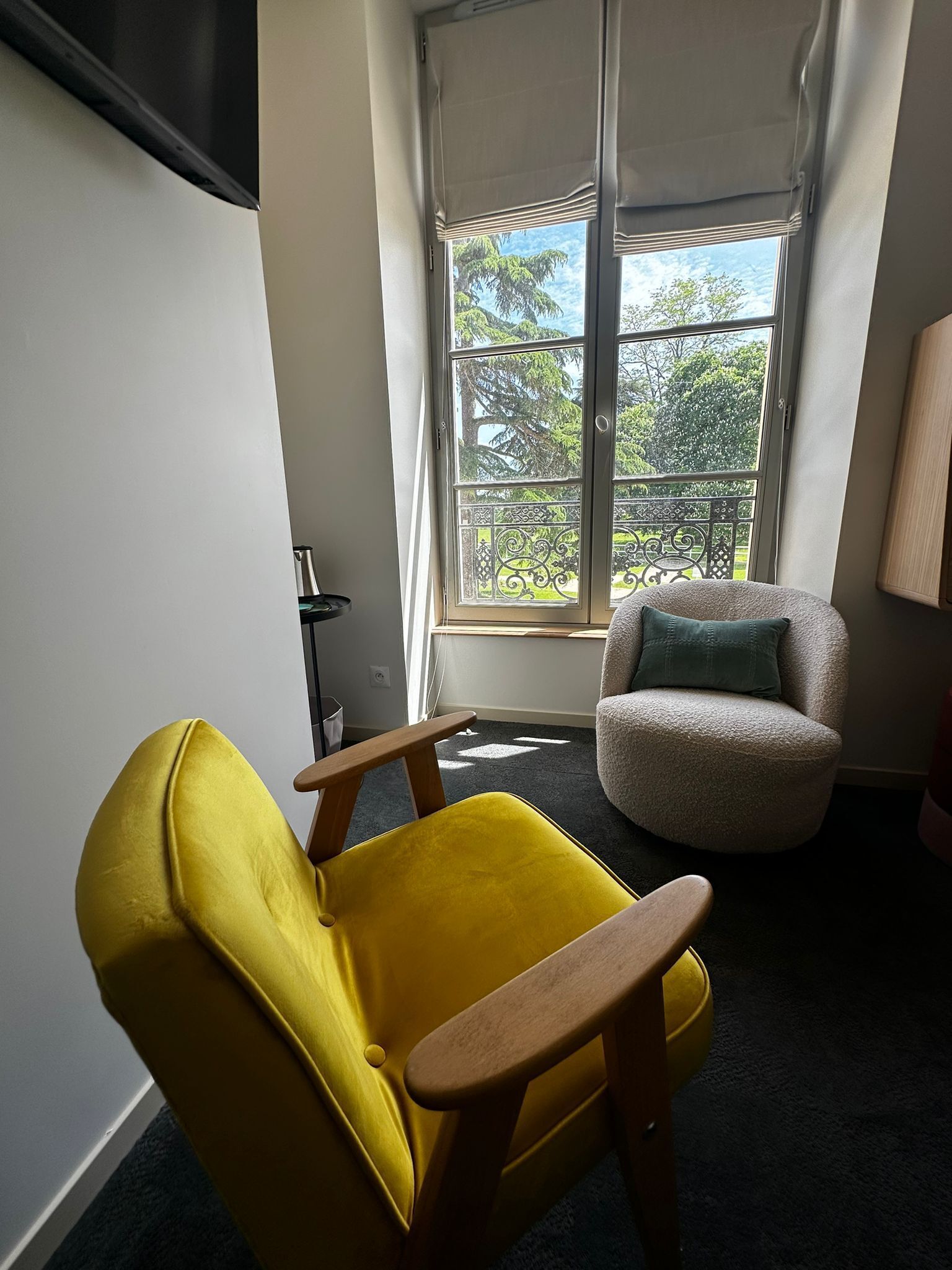 Um quarto com uma poltrona amarela, uma poltrona cinza, uma janela com vista para árvores e um abajur no chão.
