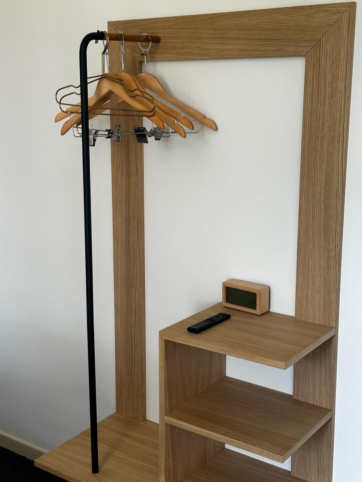 Ein Holzkleiderschrank mit Kleiderstange und einer kleinen Ablage, auf der sich eine Fernbedienung befindet.