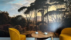 A room with a mural of a forest landscape, two yellow chairs, and a small round wooden table with two white cups. - Domaine de l'Ecorcerie (Liguge)