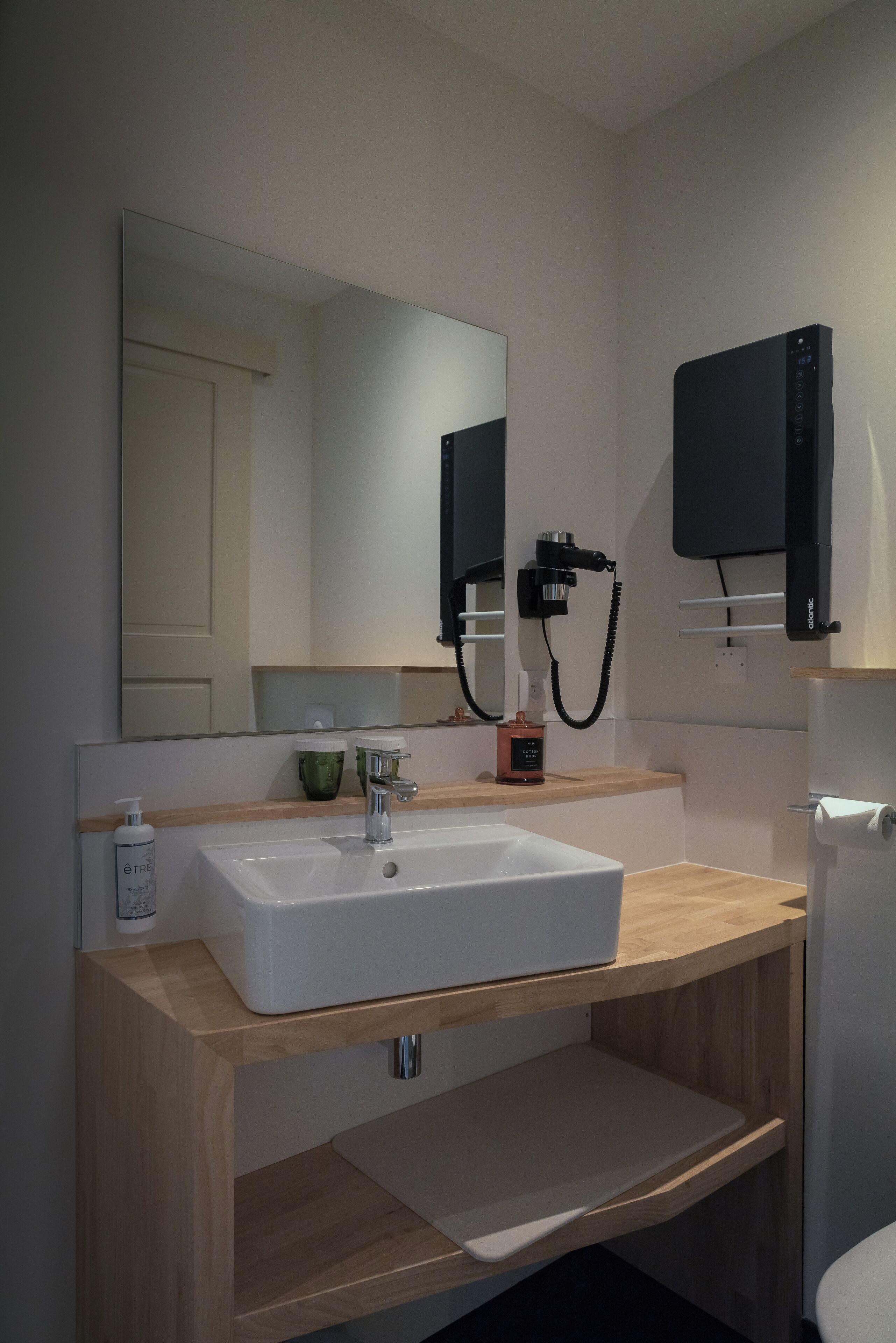 A modern bathroom with a white sink, wooden vanity, a large mirror, and a black cabinet.
