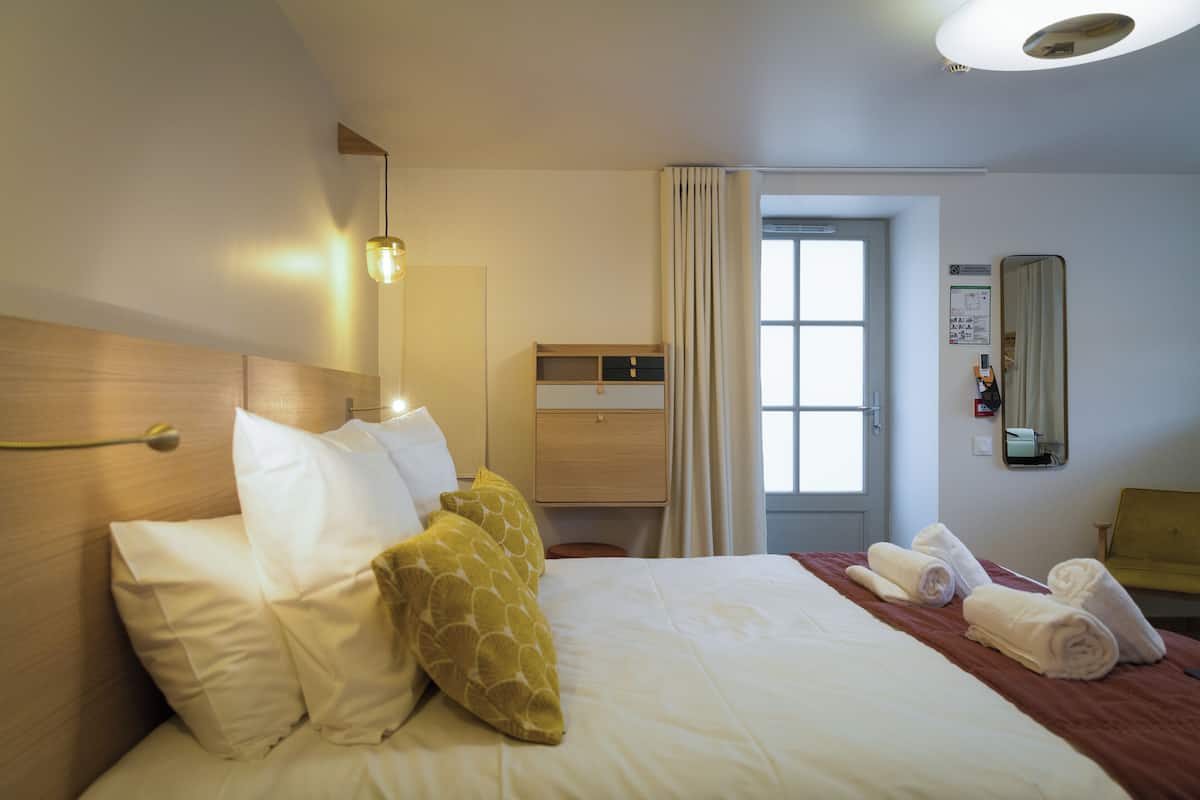 Una habitación de hotel con una cama, una mesita de noche, un espejo y una ventana con cortinas.