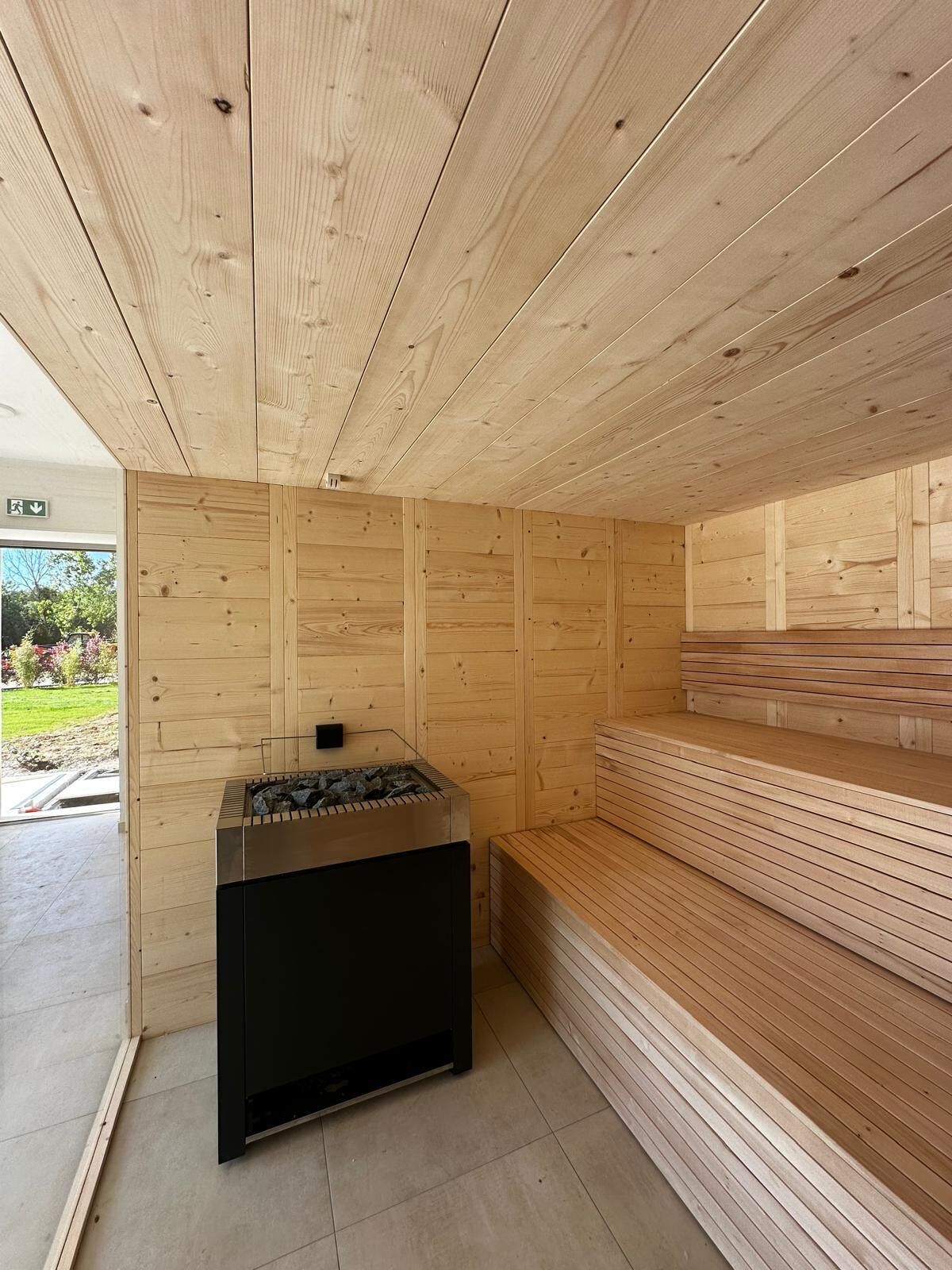 A sauna room with wooden walls and benches, a sauna unit, and a visible exit door.