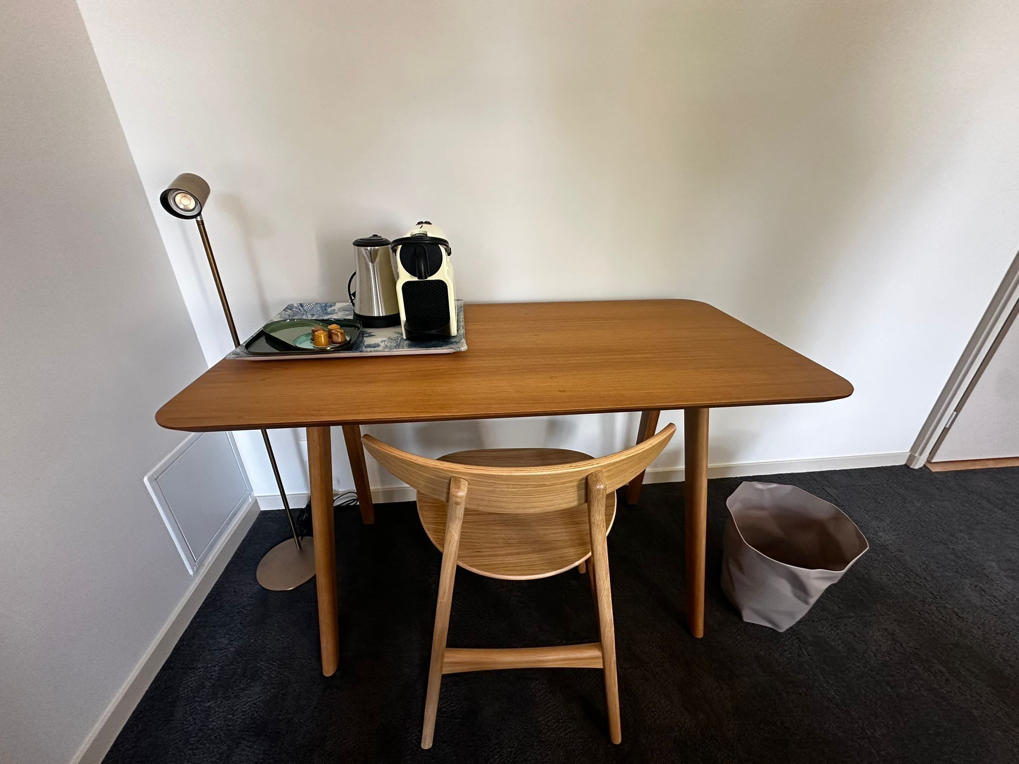 Een houten tafeltje met een stoel, een lamp, een waterkoker en een bord met eten.