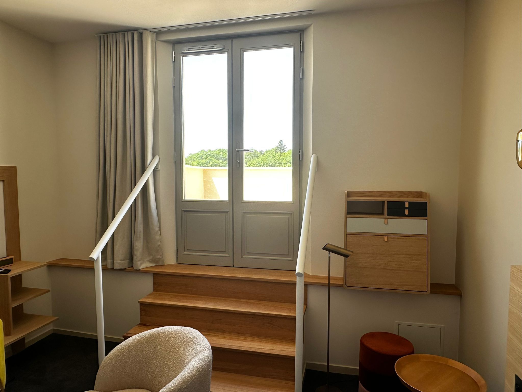 Ein Zimmer mit einer Holztreppe, einem fenster mit Vorhängen, einem Schreibtisch und einem Stuhl.