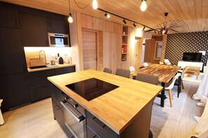 A modern kitchen with a central island, dark cabinetry, and a dining area with a wooden table and chairs. - Wifi, 300m from resort center, 2nd floor, view ski slopes, tv, ski locker, 77m², Les Gets (Les Gets)