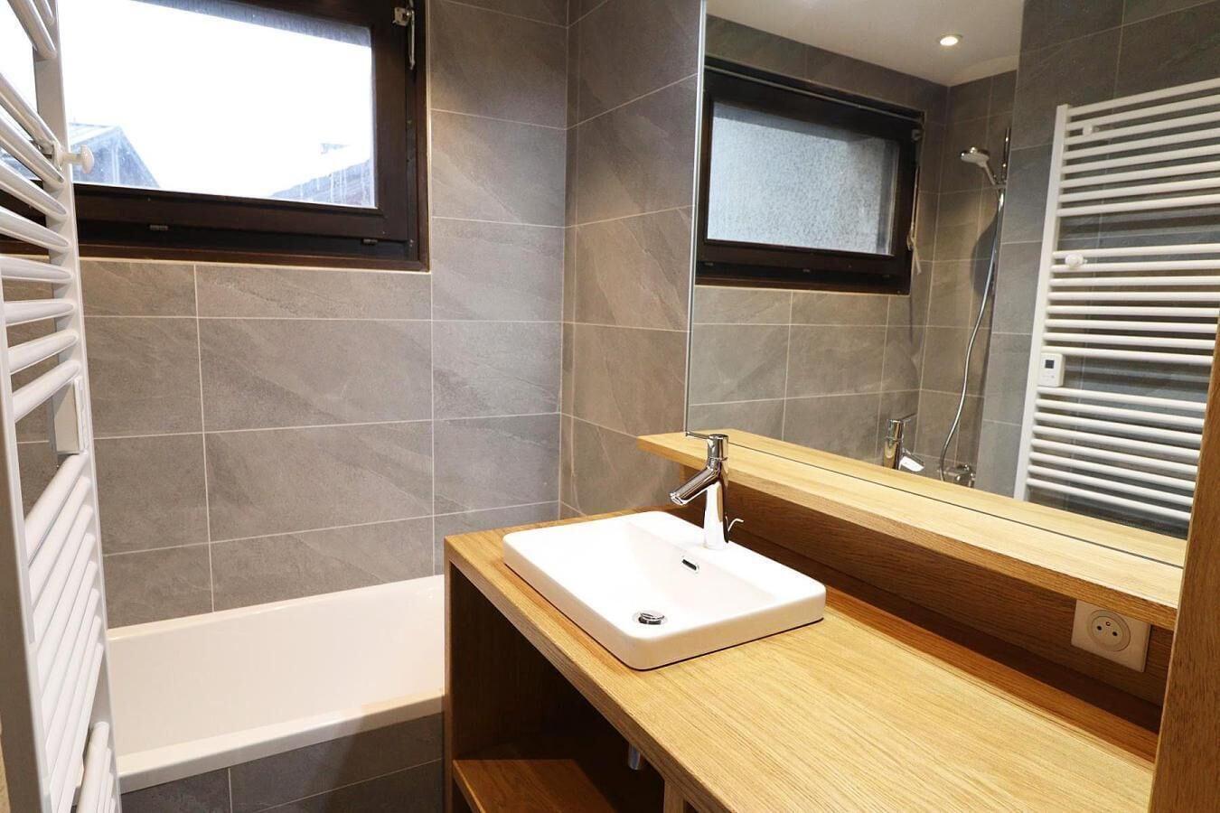 A modern bathroom with a white sink, wooden vanity, and a large mirror.