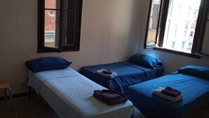 A dormitory room with three single beds, a wooden stool, and a window with a view of buildings. - 2 bedroom apartment in venice (Venezia)