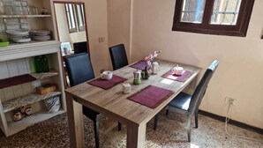 A dining area with a wooden table, black chairs, and purple placemats. There are plates and cups on the table, and a shelf with glassware and a green bottle. - 2 bedroom apartment in venice (Venezia)