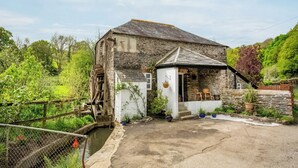 Ein rustikales Steinhaus mit einer kleinen Veranda und einem Wasserrad.