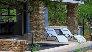 Una piscina de piedra con sillones de descanso, rodeada por un muro de piedra y vegetación.