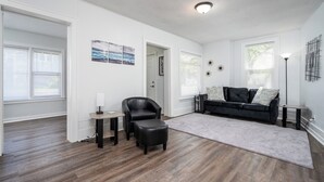 A spacious living room with hardwood flooring, a black leather chair, a gray rug, and a black sofa with pillows. - 3 bed/1 bath lower unit conveniently located in Lakeside. (Muskegon)