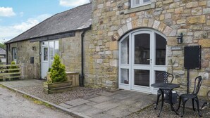A stone cottage with a large arched window, a small patio with a table and chairs, and a wooden fence. - 2 bedroom accommodation in Netherton Near Rothbury (Netherton Near Rothbury)