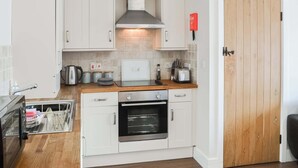 A compact kitchen with white cabinets, a stainless steel oven, a toaster, and a wooden door. - 2 bedroom accommodation in Netherton Near Rothbury (Netherton Near Rothbury)