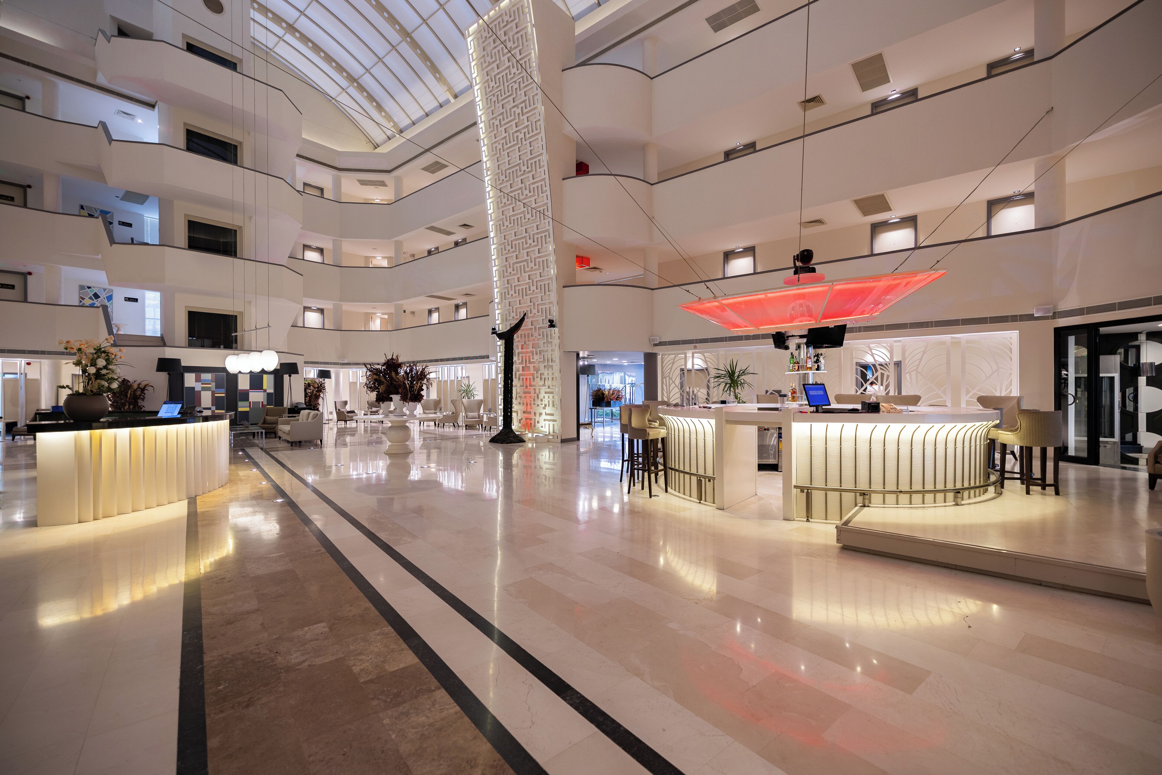 Un amplio vestíbulo de hotel de varios niveles, con una zona de recepción central, diversas opciones de asientos y un columnario geométrico distintivo.