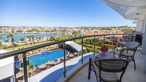 A balcony with a pool, chairs, and a table overlooking a marina and cityscape. - Sisus Marina Hotel (Cesme)
