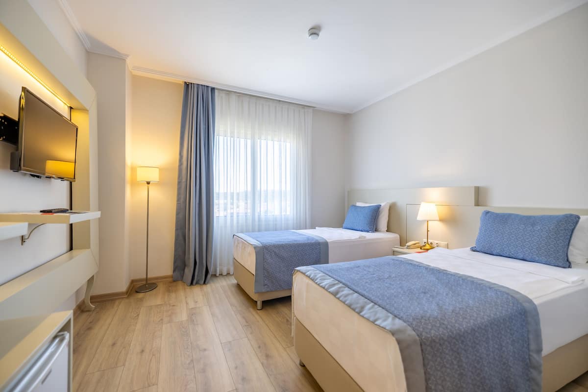 A hotel room with two beds, a TV, a desk, and a window with curtains.