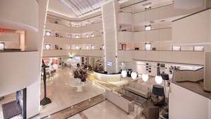 A multi-level hotel lobby with a central reception desk, multiple seating areas, and a modern architectural design. - Sisus Marina Hotel (Cesme)