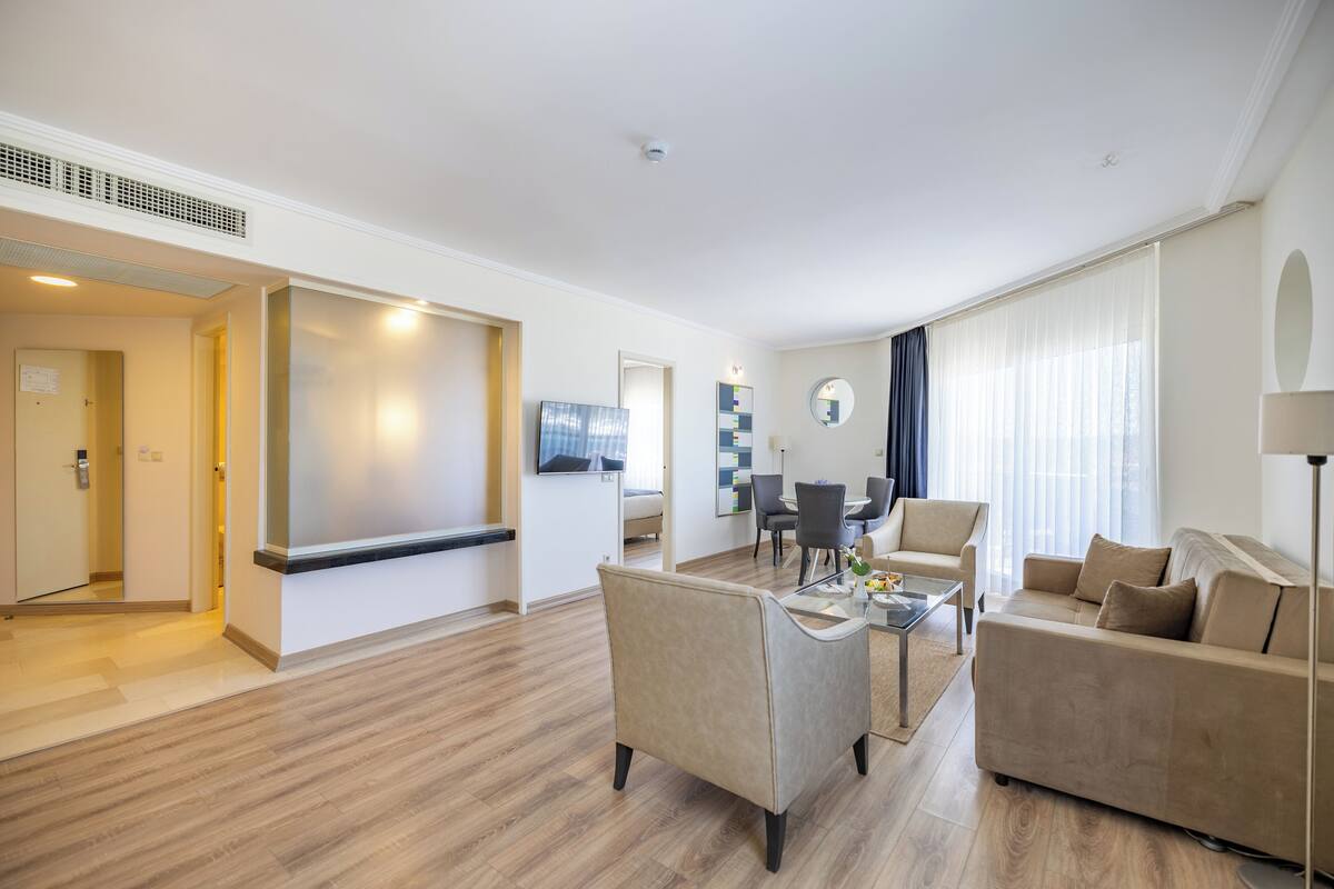 A modern hotel room with a living area, a dining table, and a sofa.