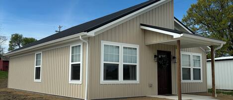 A single-story house with a beige siding exterior, a dark roof, and a front porch.