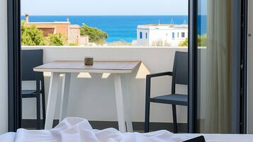 A bedroom with a laptop on a bed, a table with chairs, and a view of the sea and buildings.