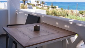 A balcony with a table and chair, overlooking a coastal area with buildings and the sea. - Filia Skyros Suites (Skiros)
