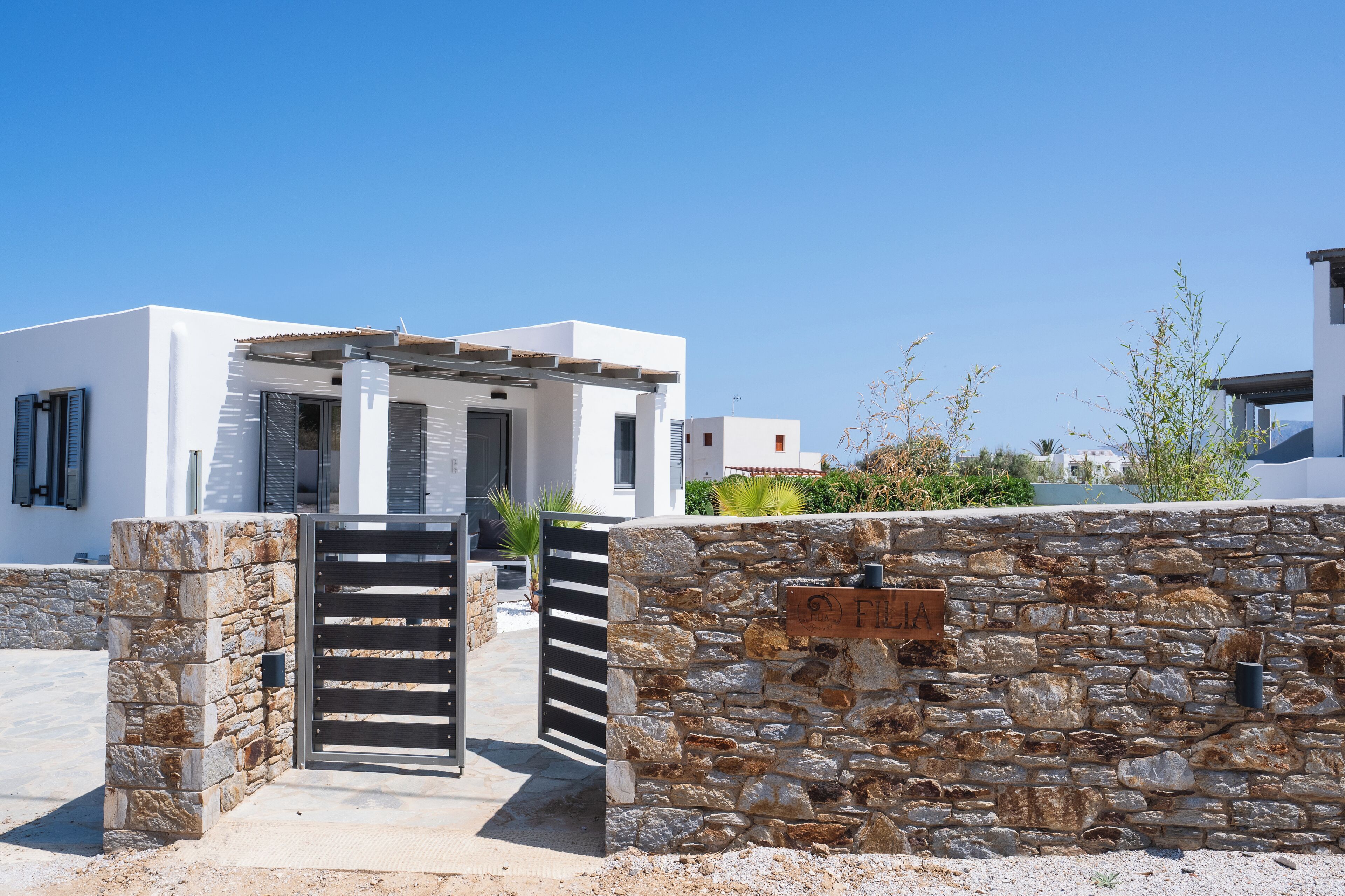 A modern villa with a stone wall entrance, a gated driveway, and a clear blue sky.