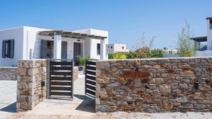 A modern villa with a stone wall entrance, a gated driveway, and a clear blue sky. - Filia Skyros Suites (Skiros)