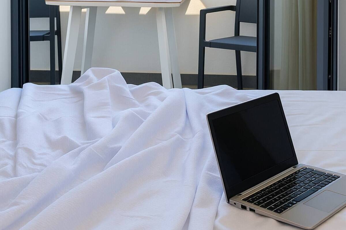 A bedroom with a laptop on a bed, a table with chairs, and a view of the sea.