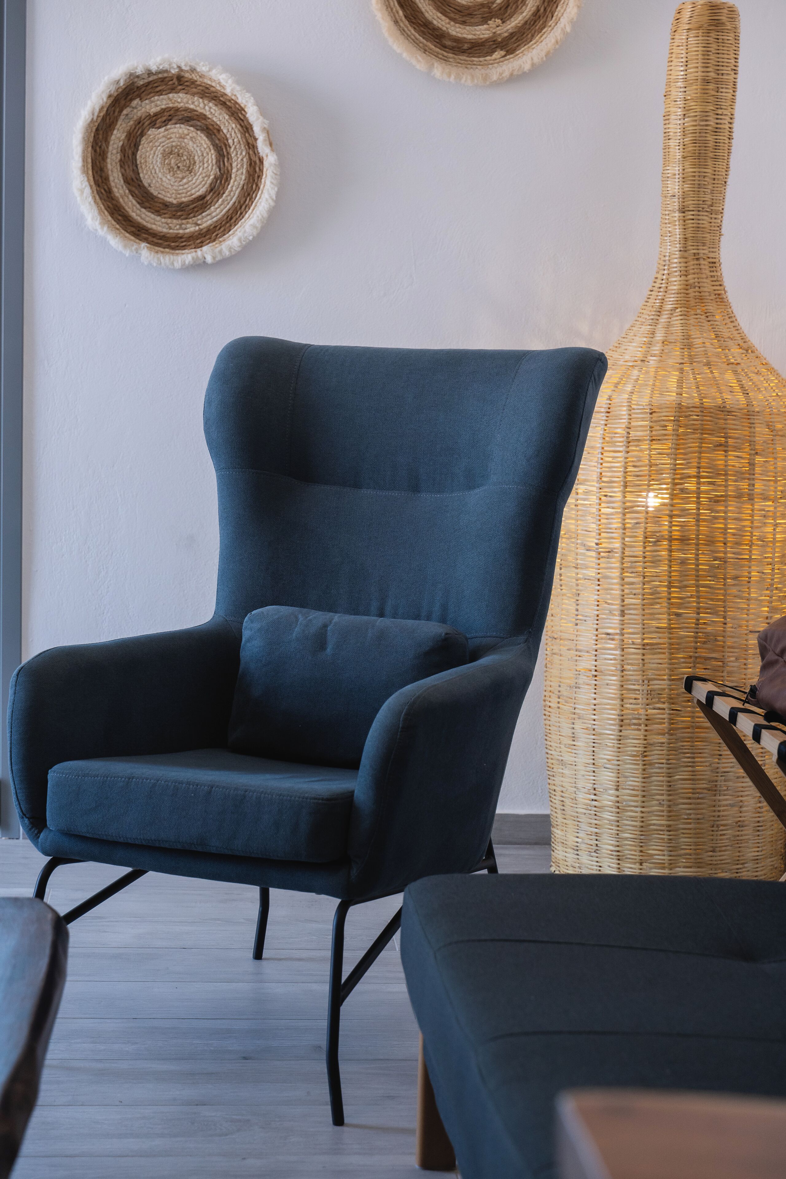A modern living room with a dark blue armchair, a wicker vase, and two circular wall decorations.
