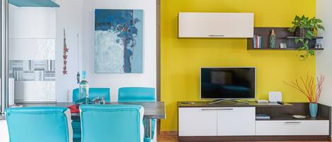 A modern living room with a dining area, a flat-screen TV, and a yellow accent wall.