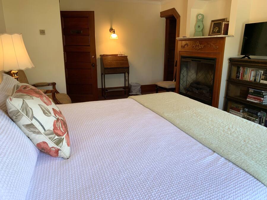 A bedroom with a bed, a nightstand, a lamp, a fireplace, and a bookshelf.