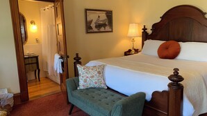 Un dormitorio ordenado con una cama de madera, un sillón verde, una mesita de noche con una lámpara y un cuadro en la pared.