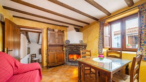 Una habitació acollidora amb una llar de foc, bigues de fusta, una taula de menjador amb cadires i un sofà vermell.