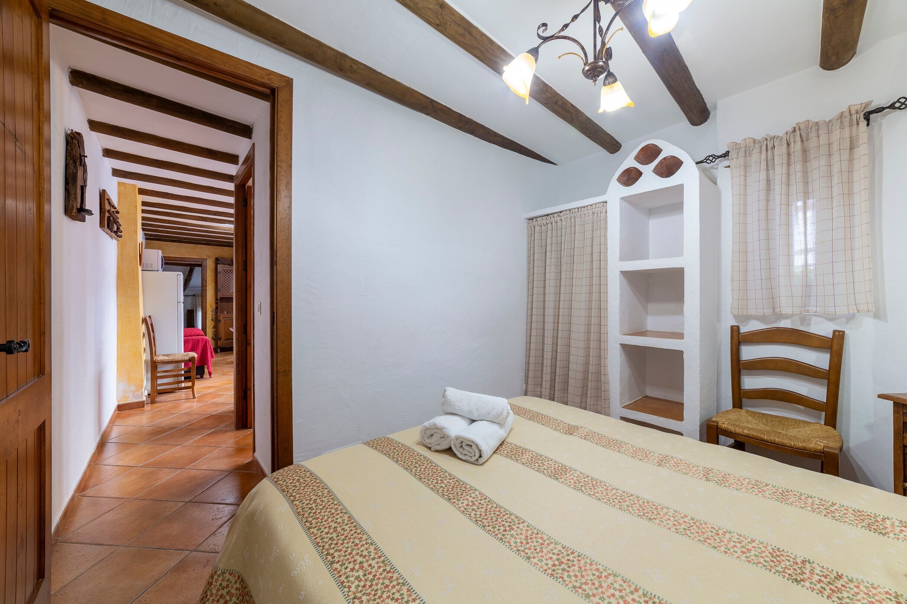 Une chambre à coucher comprenant un lit, une chaise en bois, une armoire et une porte donnant sur une autre pièce.