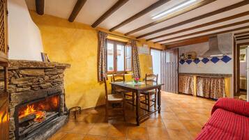 Una habitación acogedora con chimenea de piedra, vigas de madera, una mesa de comedor con sillas y un sofá rojo.